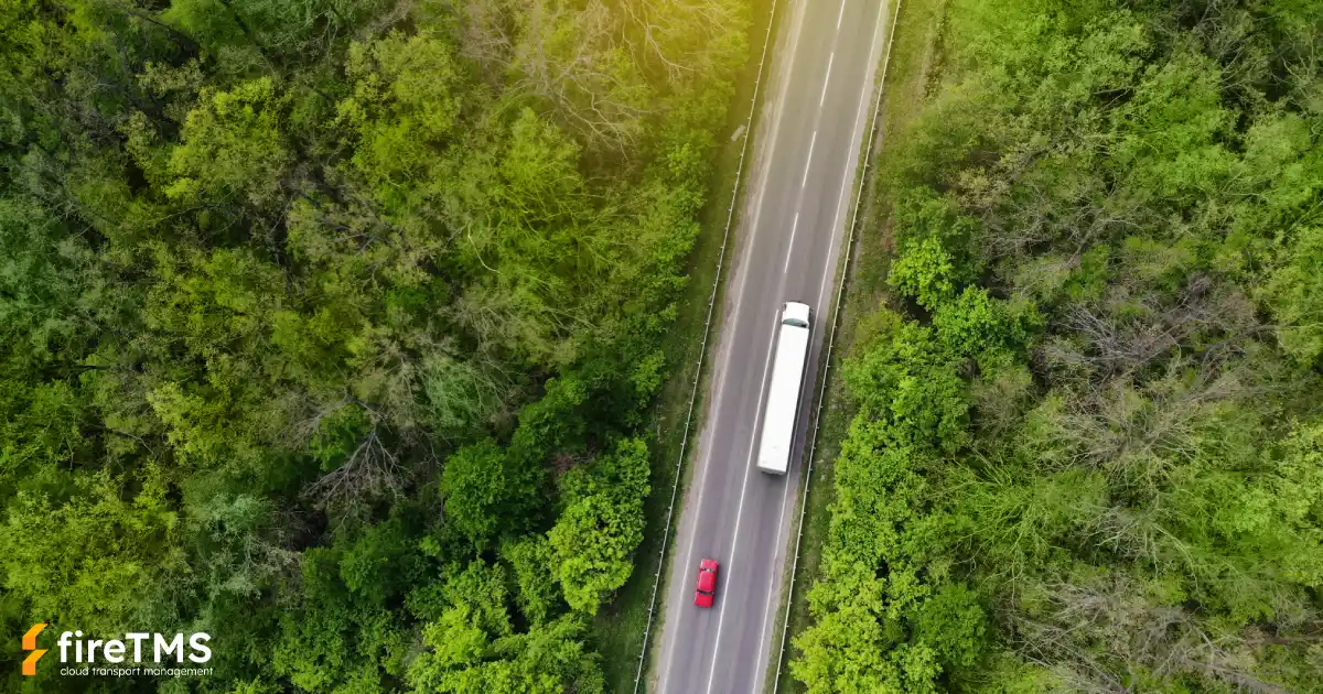Widok z lotu ptaka na drogę przechodzącą przez las. Na drodze widać zestaw transportowy i samochód osobowy