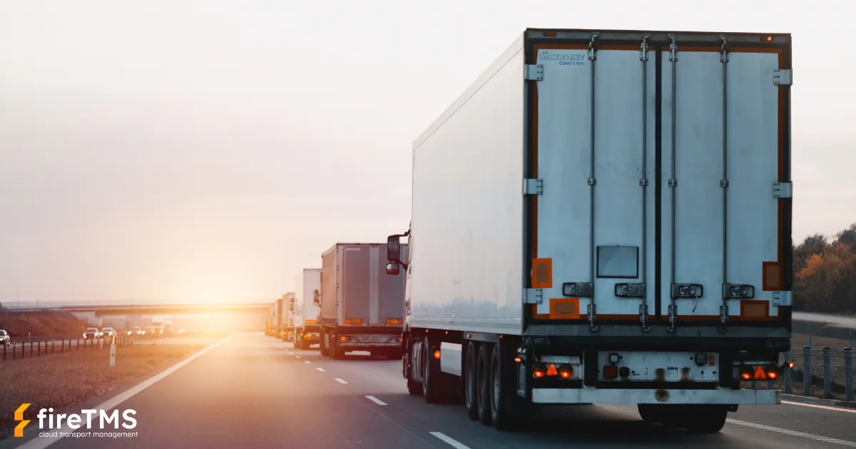 Samochody ciężarowe i zestawy transportowe jadą jeden za drugim autostradą przy zachodzącym słońcu